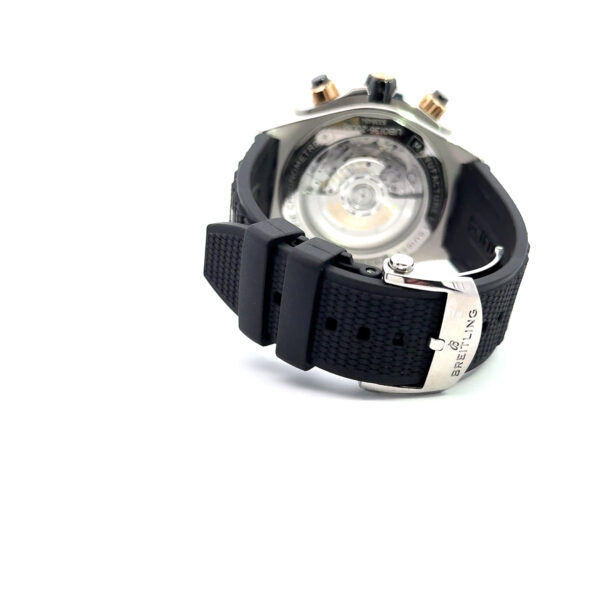 Die Breitling Super Chronomat B01 44 ist eine Luxusuhr mit schwarzem Kautschukarmband, einem Ausstellungsboden, auf dem das mechanische Uhrwerk zu sehen ist, und einer Schließe mit der Gravur "BREITLING" auf weißem Grund.
