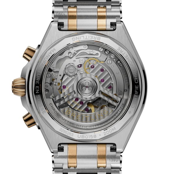 Die Nahaufnahme des Bodens der Breitling Chronomat II B01 Chronograph 42 offenbart ihr komplexes mechanisches Uhrwerk durch einen transparenten Gehäuseboden. Das Metallarmband besteht aus silber- und goldfarbenen Gliedern, auf denen die technischen Daten eingraviert sind.
