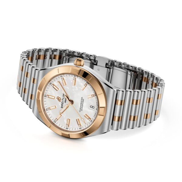 Die Breitling Chronomat II Automatic 36 verfügt über ein silbernes und goldenes Metallband, ein rundes weißes Perlmuttzifferblatt, goldene Indexe und Zeiger, ein Datumsfenster bei 6 Uhr und das Breitling-Logo auf dem Zifferblatt.