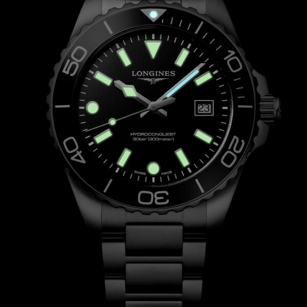Die Longines HydroConquest Quarz ist eine Armbanduhr aus schwarzem Metall mit rundem Zifferblatt, grün leuchtenden Indexen und Zeigern, einer drehbaren Lünette sowie einem Datumsfenster bei 3 Uhr auf einem schwarzen Zifferblatt mit dem Longines-Logo.