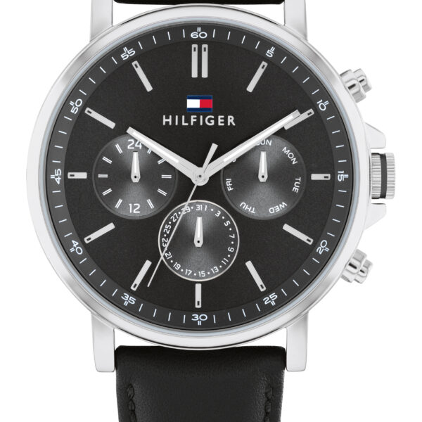 Die Tommy Hilfiger Tyson ist eine Armbanduhr aus schwarzem Leder mit einem schwarzen Zifferblatt, das drei Hilfszifferblätter, silberne Indizes und das Hilfiger-Logo unterhalb der 12-Uhr-Markierung aufweist. Sie verfügt über ein silbernes Gehäuse, das auf der rechten Seite mit zwei Drückern und einer Krone ausgestattet ist.
