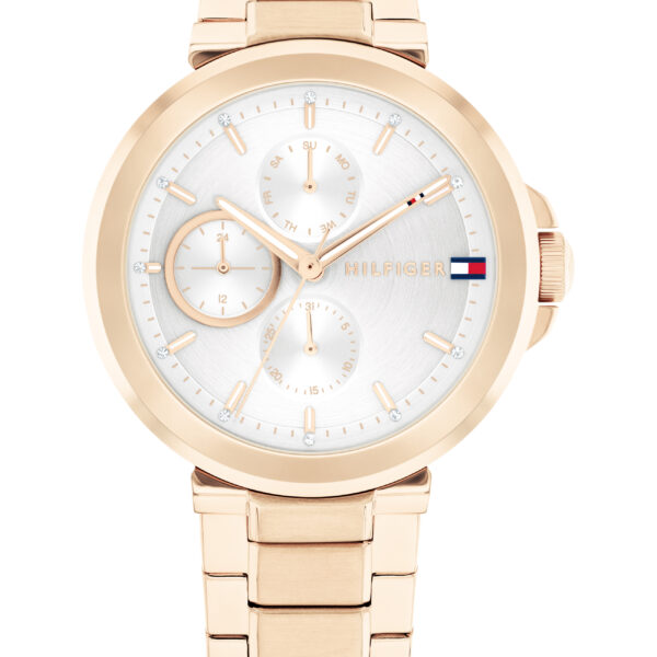 Die Tommy Hilfiger Lori Armbanduhr verfügt über ein goldfarbenes Metallgliederarmband, ein weißes Zifferblatt mit drei Hilfszifferblättern, goldene Stundenindizes und das Tommy Hilfiger-Flaggenlogo auf der rechten Seite des Zifferblatts.