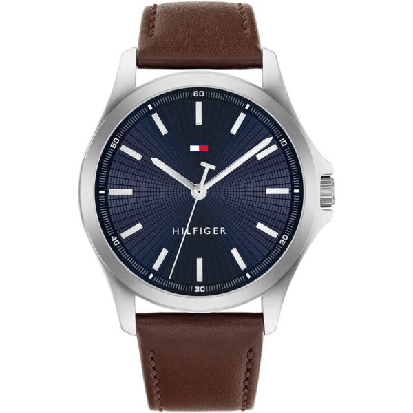 Die Tommy Hilfiger Bruce ist eine Armbanduhr mit einem braunen Lederarmband, einem silbernen Gehäuse und einem dunkelblauen Zifferblatt mit weißen Indexen, drei Zeigern und einem kleinen rechteckigen Logo in den Farben Rot, Weiß und Blau nahe der 12-Uhr-Position.