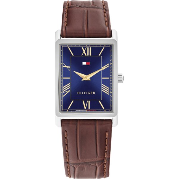 Die Tommy Hilfiger Ben ist eine rechteckige Uhr mit einem blauen Zifferblatt mit goldenen römischen Ziffern und Zeigern, einem braunen Lederarmband und einem kleinen rot-weiß-blauen Tommy Hilfiger-Logo unterhalb der 12-Uhr-Markierung.