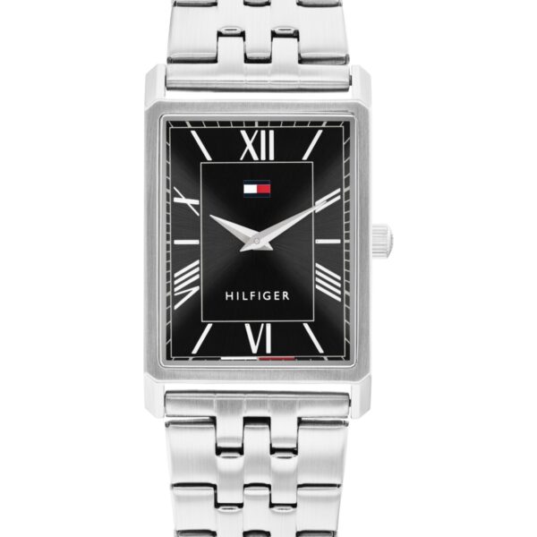 Eine rechteckige silberfarbene Tommy Hilfiger Ben-Armbanduhr mit schwarzem Zifferblatt und weißen römischen Ziffern, einem Metallarmband und dem Tommy Hilfiger-Logo unterhalb der 12-Uhr-Markierung. Die Stunden- und Minutenzeiger sind silberfarben.