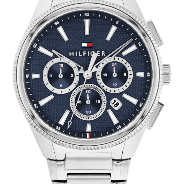 Wir präsentieren die Sam Multifunktion: eine silberne Armbanduhr mit blauem, strukturiertem Zifferblatt, drei Hilfszifferblättern, silbernen Indexen und dem Hilfiger-Logo oben am Zifferblatt. Das Metallarmband besticht durch seine polierte Oberfläche.