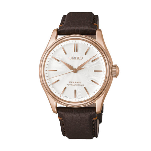 Die Seiko Presage X Tomioka Silk Limited Edition verfügt über ein weißes Zifferblatt, ein roségoldfarbenes Gehäuse und ein braunes Lederarmband. Die Uhr ist mit goldenen Indexen und Zeigern verziert, während auf dem Zifferblatt die Aufschriften „SEIKO“ und „PRESAGE AUTOMATIC 3 DAYS“ zu sehen sind.