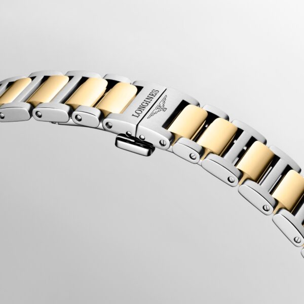 Nahaufnahme eines Metallarmbands mit abwechselnden goldenen und silbernen Gliedern, auf dessen Verschluss vor hellem Hintergrund der Name „Longines Conquest“ und das Symbol der geflügelten Sanduhr eingraviert sind.
