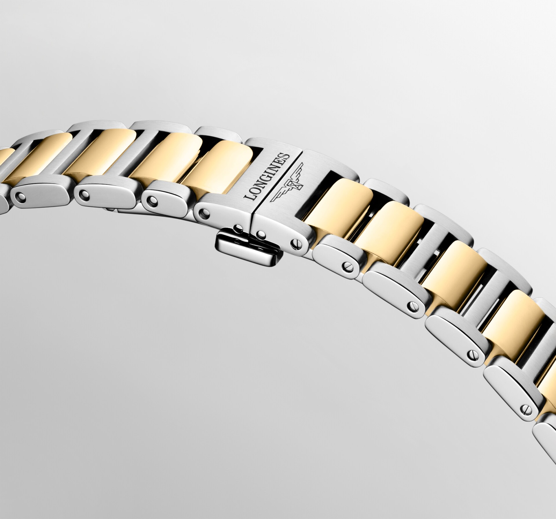 Nahaufnahme eines Metallarmbands mit abwechselnden goldenen und silbernen Gliedern, auf dessen Verschluss vor hellem Hintergrund der Name „Longines Conquest“ und das Symbol der geflügelten Sanduhr eingraviert sind.