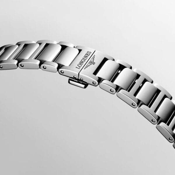 Eine Nahaufnahme des silbernen Metallarmbands der Longines Conquest, auf dessen einem Glied das „LONGINES“-Logo und das Symbol der geflügelten Sanduhr eingraviert sind, vor einem hellgrauen Hintergrund.