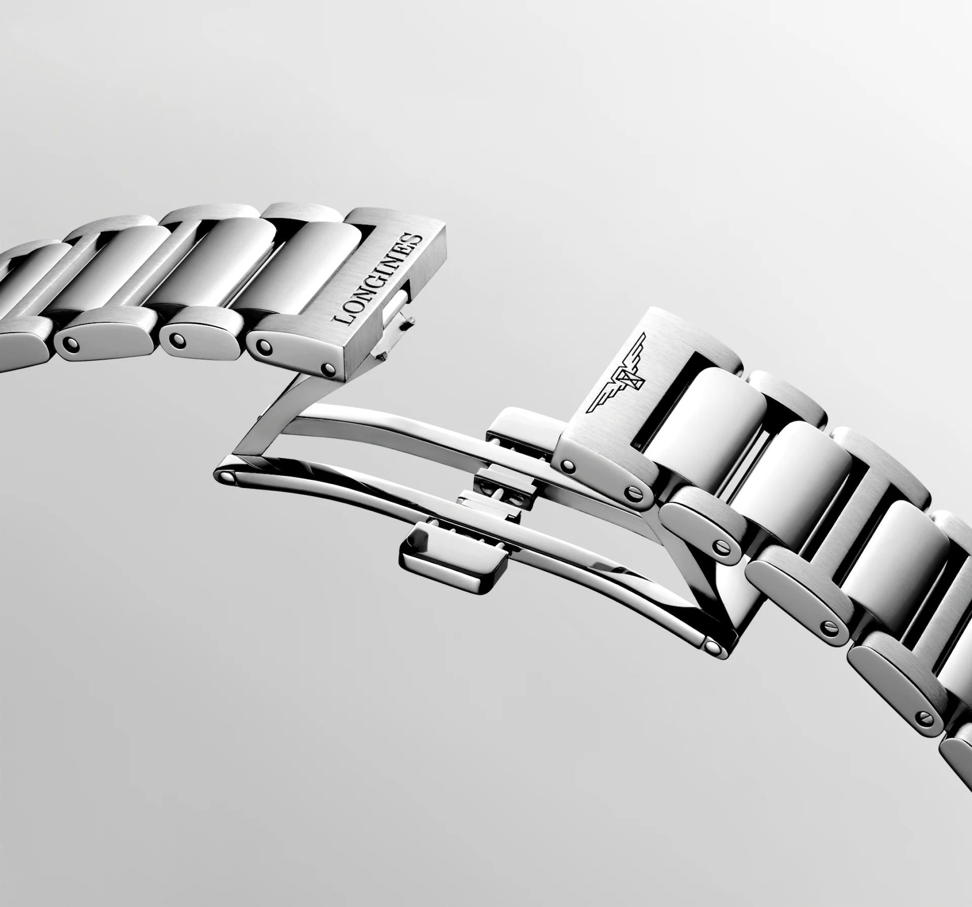 Eine Nahaufnahme des silbernen Metallarmbands der Longines Conquest mit Faltschließe, auf dessen polierten Gliedern das Longines-Logo und gravierte Details vor einem hellen Hintergrund zu sehen sind.