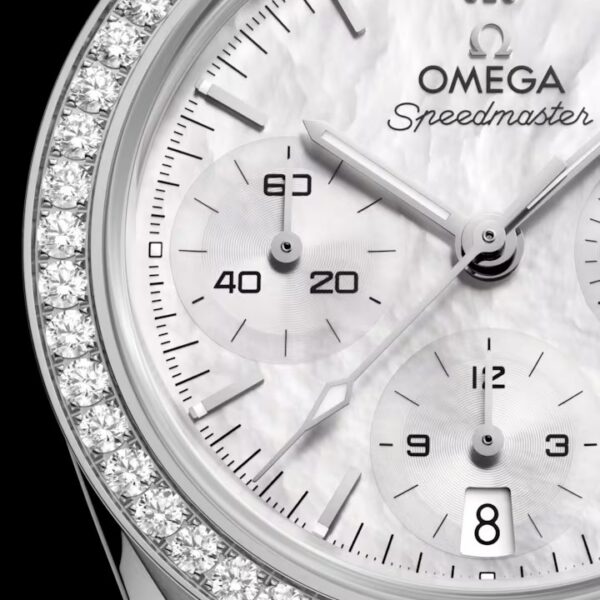 Nahaufnahme der OMEGA Speedmaster 38 mit weißem Zifferblatt, drei Hilfszifferblättern, Datumsfenster und einer mit funkelnden Diamanten verzierten Lünette. Silberne Zeiger und Indizes heben sich deutlich vom fein strukturierten Zifferblatt ab.