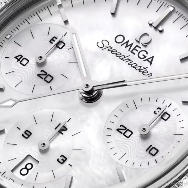 Nahaufnahme des Zifferblatts einer OMEGA Speedmaster 38 mit drei Hilfszifferblättern, einer Diamantlünette und silbernen Zeigern auf weißem Hintergrund. Der Schriftzug „Speedmaster“ ist deutlich unterhalb des OMEGA-Logos zu sehen.