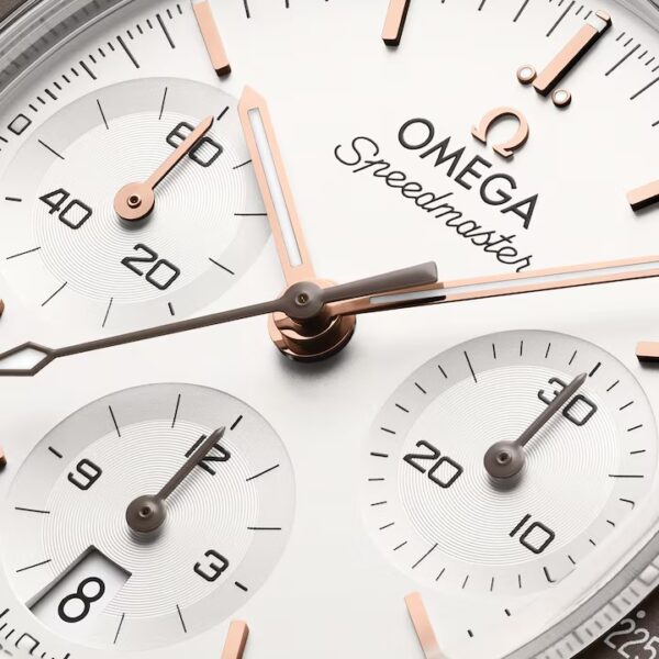 Nahaufnahme des Zifferblatts einer OMEGA Speedmaster 38 mit roségoldenen Zeigern, drei Hilfszifferblättern und schwarzen Indexen auf weißem Hintergrund. Der Markenname „Omega Speedmaster“ ist zu sehen.