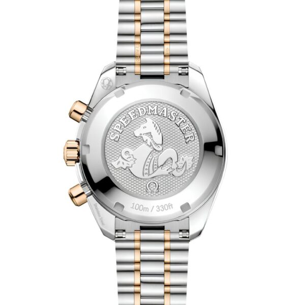 Auf der Rückseite der OMEGA Speedmaster 38 sind eine Drachengravur, goldene Knöpfe und ein zweifarbiges Metallarmband in Silber und Gold zu sehen. Die Gravur enthält die Aufschriften „SPEEDMASTER“ und „100 m / 330 ft“.