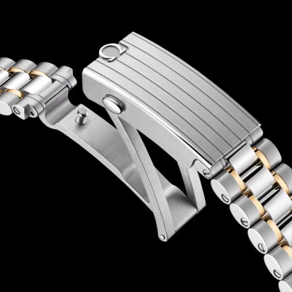 Nahaufnahme des Verschlusses des Metallarmbands der OMEGA Speedmaster 38 mit abwechselnd silbernen und goldenen Gliedern, offen vor schwarzem Hintergrund.