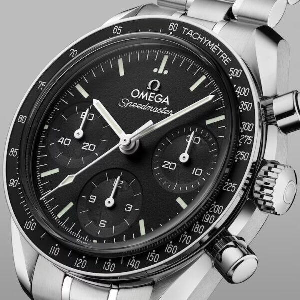 Eine Nahaufnahme der OMEGA Speedmaster 38 Armbanduhr mit schwarzem Zifferblatt, drei Hilfszifferblättern, einer Tachymeter-Lünette und einem Edelstahlarmband vor grauem Hintergrund.
