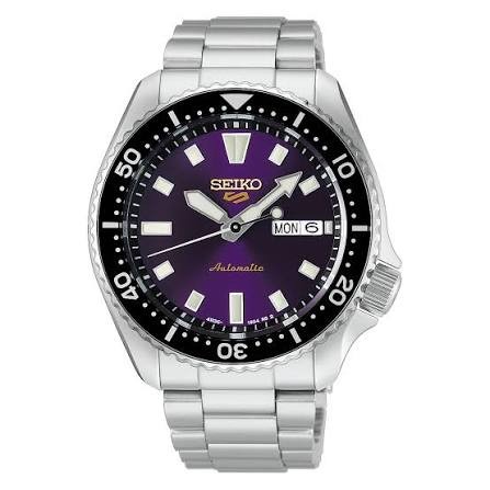 Analoge Seiko 5 Sports Limited Edition-Armbanduhr mit einem silbermetallischen Gliederarmband, einer schwarzen drehbaren Lünette und einem tiefvioletten Zifferblatt mit Wochentags- und Datumsanzeige.